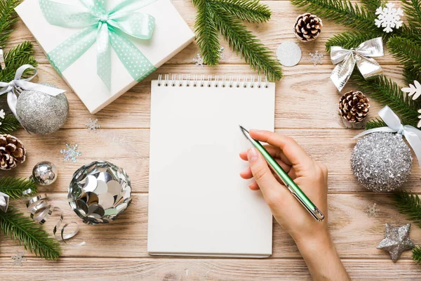 stock image Woman writing Christmas to do list on notebook on colored background with xmas decorations.