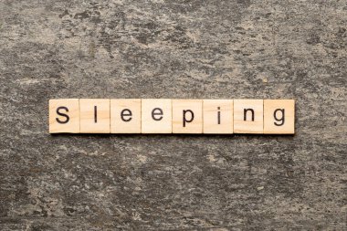 Tahta blokta uyku kelimesi yazıyor. Deksing, konsept için çimento masanın üzerinde uyuyan metin.