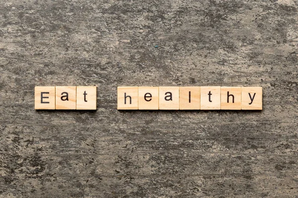 木のブロックに書かれた健康的な言葉を食べる あなたのデザイン コンセプトのためのセメントテーブル上の健康的なテキストを食べる — ストック写真