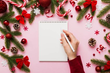 Noel 'i yazmak için bir kadın not defterine Xmas dekorasyonlu renkli arkaplan çiziyor.