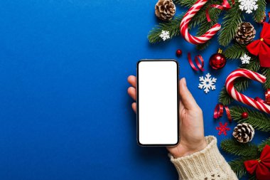 Mesaj atmak için yeri olan bir Noel modeli. Noel reklamı, uygulama şablonu. Masa arkasında boş ekran olan el ele tutuşan telefon. Mutlu yıllar ve Xmas Flat.