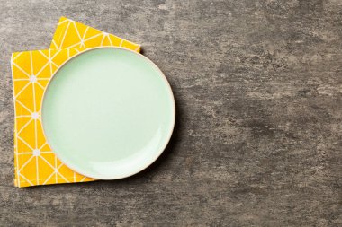 Renkli arka planda üst görünüm yiyecek için masa örtüsünün üzerinde boş yuvarlak yeşil tabak. Tasarımınız için boşluk olan peçeteye boş tabak.