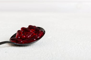 Renkli bir arka planda kaşıkta vitamin kapsülleri. Haplar sağlıklı bir yemek olarak sunuldu. Kırmızı yumuşak jel vitamin takviye kapsülleri kaşık üzerinde.