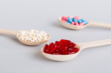 Renkli bir arka planda kaşıkta vitamin kapsülleri. Haplar sağlıklı bir yemek olarak sunuldu. Kırmızı yumuşak jel vitamin takviye kapsülleri kaşık üzerinde.