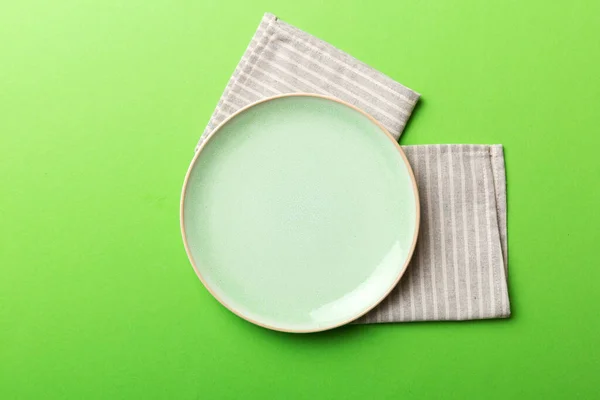 テーブルクロスの色の背景の空の丸い緑のプレートの上からの眺め あなたのデザインのためのスペースとナプキンに空の料理 — ストック写真