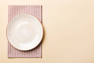 Renkli arka planda üst görünüm yiyecek için masa örtüsü üzerindeki boş yuvarlak beyaz tabak. Tasarımınız için boşluk olan peçeteye boş tabak.