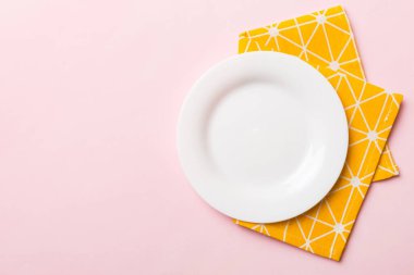 Renkli arka planda üst görünüm yiyecek için masa örtüsü üzerindeki boş yuvarlak beyaz tabak. Tasarımınız için boşluk olan peçeteye boş tabak.