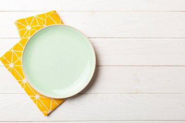 Renkli arka planda üst görünüm yiyecek için masa örtüsünün üzerinde boş yuvarlak yeşil tabak. Tasarımınız için boşluk olan peçeteye boş tabak.