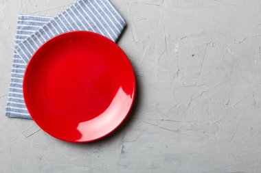 Renkli arka planda üst görünüm yiyecek için masa örtüsü üzerindeki boş yuvarlak kırmızı tabak. Tasarımınız için boşluk olan peçeteye boş tabak.