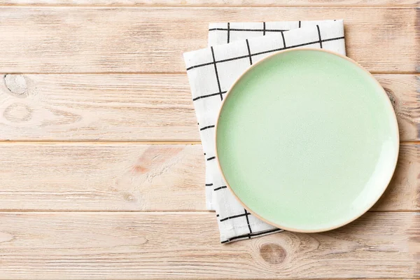 テーブルクロスの色の背景の空の丸い緑のプレートの上からの眺め あなたのデザインのためのスペースとナプキンに空の料理 — ストック写真