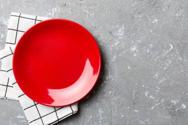 Renkli arka planda üst görünüm yiyecek için masa örtüsü üzerindeki boş yuvarlak kırmızı tabak. Tasarımınız için boşluk olan peçeteye boş tabak.