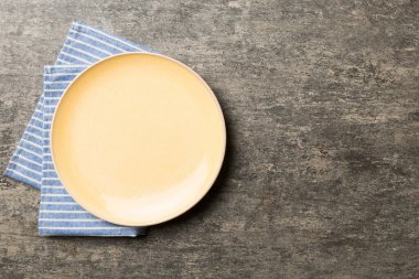 Renkli arka planda üst manzara. Yemek için masa örtüsü üzerinde boş yuvarlak sarı tabak. Tasarımınız için boşluk olan peçeteye boş tabak.