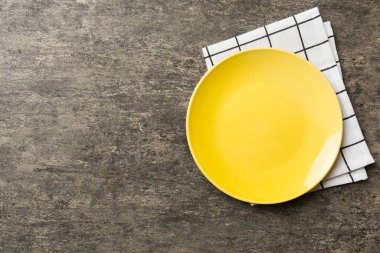 Renkli arka planda üst manzara. Yemek için masa örtüsü üzerinde boş yuvarlak sarı tabak. Tasarımınız için boşluk olan peçeteye boş tabak.