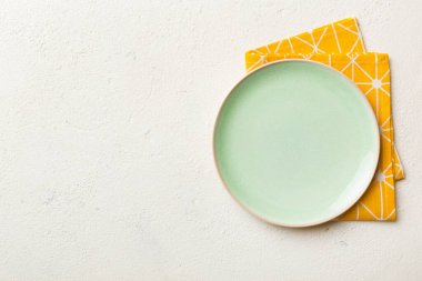 Renkli arka planda üst görünüm yiyecek için masa örtüsünün üzerinde boş yuvarlak yeşil tabak. Tasarımınız için boşluk olan peçeteye boş tabak.