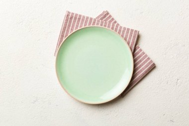 Renkli arka planda üst görünüm yiyecek için masa örtüsünün üzerinde boş yuvarlak yeşil tabak. Tasarımınız için boşluk olan peçeteye boş tabak.