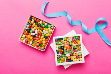 Renkli bir arka planda saten bir kurdeleyle karton kutuda farklı şekerler. Tatil kavramı.