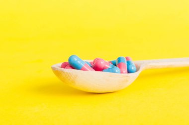 Renkli bir arka planda kaşıkta vitamin kapsülleri. Haplar sağlıklı bir yemek olarak sunuldu. Kırmızı yumuşak jel vitamin takviye kapsülleri kaşık üzerinde.