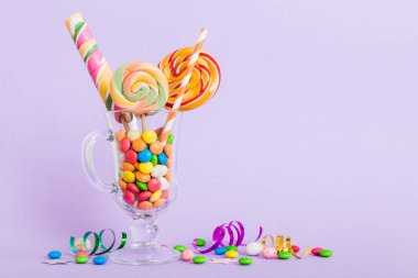 Masanın üzerinde açık arkaplanda renkli şekerler. Büyük kıvrımlı lolipoplar. Şekerci dükkanından leziz şekerlerle dolu yaratıcı bir kavanoz konsepti.