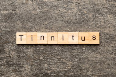 Tahta bloğa yazılmış bir kelime. Çimento sehpası üzerindeki TINNITUS metin desing, konsept.