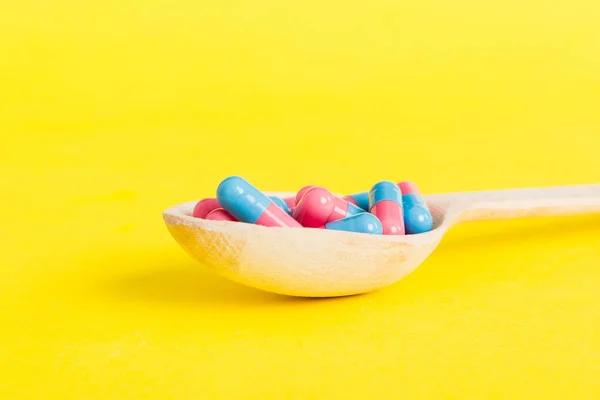 Stock image Vitamin capsules in a spoon on a colored background. Pills served as a healthy meal. Red soft gel vitamin supplement capsules on spoon.