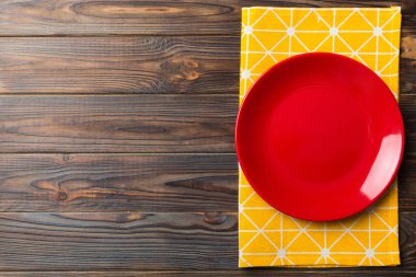 Renkli arka planda üst görünüm yiyecek için masa örtüsü üzerindeki boş yuvarlak kırmızı tabak. Tasarımınız için boşluk olan peçeteye boş tabak.