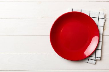Renkli arka planda üst görünüm yiyecek için masa örtüsü üzerindeki boş yuvarlak kırmızı tabak. Tasarımınız için boşluk olan peçeteye boş tabak.