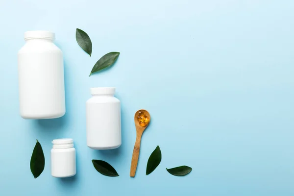 Omega-3 capsules lie in white bottle on a table with green leaves background. Fish oil tablets. Biologically active additives. omega 6, omega 9, vitamin A, E, D, vitamin D3 top view with copy space.