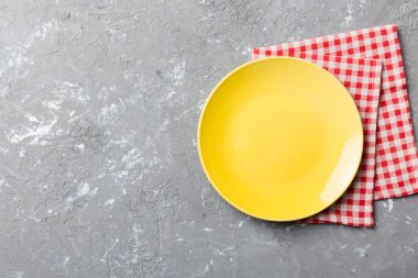 Renkli arka planda üst manzara. Yemek için masa örtüsü üzerinde boş yuvarlak sarı tabak. Tasarımınız için boşluk olan peçeteye boş tabak.