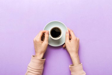 Renkli arka planda bir fincan kahve tutan minimalist stil bir kadın. Düz yatıyordu, üstten espresso fincanı. Metin için boş yer, kopyalama alanı. Kahve bağımlılığı. Üst manzara, düz uzanma.