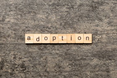 Evlat edinme kelimesi tahta blokta yazılı. Evlat edinme metni masa üzerinde, konsept.