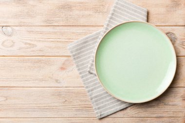 Renkli arka planda üst görünüm yiyecek için masa örtüsünün üzerinde boş yuvarlak yeşil tabak. Tasarımınız için boşluk olan peçeteye boş tabak.