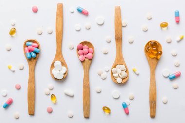 Renkli bir arka planda kaşıkta vitamin kapsülleri. Haplar sağlıklı bir yemek olarak sunuldu. Kırmızı yumuşak jel vitamin takviye kapsülleri kaşık üzerinde.