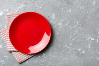 Renkli arka planda üst görünüm yiyecek için masa örtüsü üzerindeki boş yuvarlak kırmızı tabak. Tasarımınız için boşluk olan peçeteye boş tabak.