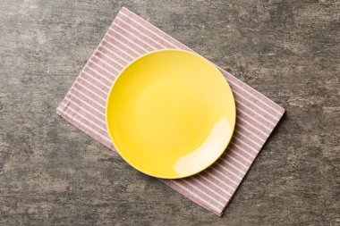 Renkli arka planda üst manzara. Yemek için masa örtüsü üzerinde boş yuvarlak sarı tabak. Tasarımınız için boşluk olan peçeteye boş tabak.
