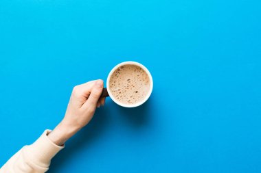 Renkli arka planda bir fincan kahve tutan minimalist stil bir kadın. Düz yerde, kapuçino bardağının üstünde. Metin için boş yer, kopyalama alanı. Kahve bağımlılığı. Üst manzara, düz uzanma.