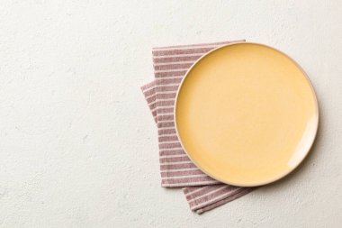 Renkli arka planda üst manzara. Yemek için masa örtüsü üzerinde boş yuvarlak sarı tabak. Tasarımınız için boşluk olan peçeteye boş tabak.