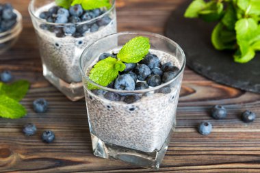 Sağlıklı kahvaltı ve chia tohumlu vanilyalı puding ve böğürtlenli masa arkası, vejetaryen gıda, diyet ve sağlık konsepti. Hindistan cevizi sütü ve yabanmersinli Chia pudingi..