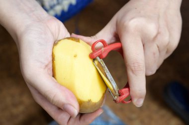 Kadın mutfakta bir sandalyede otururken patates soyuyor..