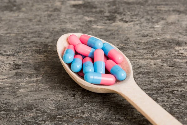 Vitamin capsules in a spoon on a colored background. Pills served as a healthy meal. Red soft gel vitamin supplement capsules on spoon.