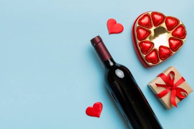 Sevgililer Günü için renkli arka planda bir şişe kırmızı şarap hediye ve çikolatalı. Kalp, hediye kutusuyla şekillendirilmiş çikolatalar fotokopi alanı ile üst görünüm.