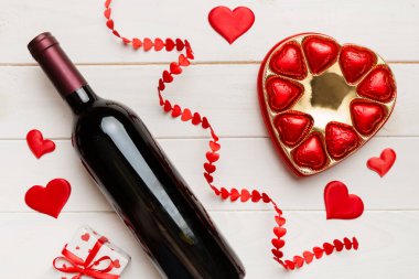 Sevgililer Günü için renkli arka planda bir şişe kırmızı şarap hediye ve çikolatalı. Kalp, hediye kutusuyla şekillendirilmiş çikolatalar fotokopi alanı ile üst görünüm.
