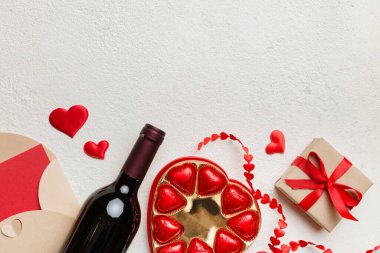 Sevgililer Günü için renkli arka planda bir şişe kırmızı şarap hediye kutusu, zarf ve çikolatalı. Kalp, hediye kutusuyla şekillendirilmiş çikolatalar fotokopi alanı ile üst görünüm.