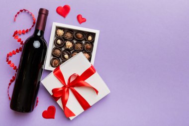 Sevgililer Günü için renkli arka planda bir şişe kırmızı şarap hediye ve çikolatalı. Kalp, hediye kutusuyla şekillendirilmiş çikolatalar fotokopi alanı ile üst görünüm.