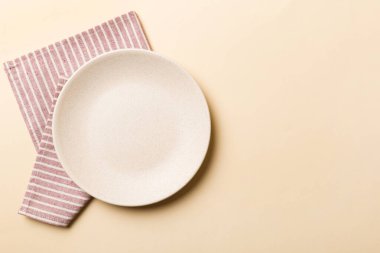 Renkli arka planda üst görünüm yiyecek için masa örtüsü üzerindeki boş yuvarlak beyaz tabak. Tasarımınız için boşluk olan peçeteye boş tabak.