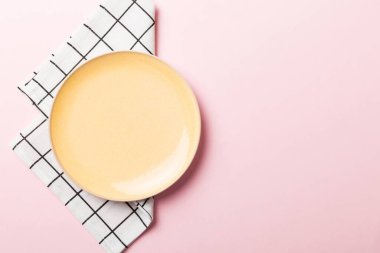 Renkli arka planda üst manzara. Yemek için masa örtüsü üzerinde boş yuvarlak sarı tabak. Tasarımınız için boşluk olan peçeteye boş tabak.