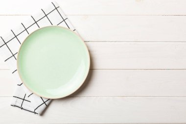 Renkli arka planda üst görünüm yiyecek için masa örtüsünün üzerinde boş yuvarlak yeşil tabak. Tasarımınız için boşluk olan peçeteye boş tabak.