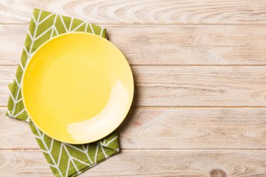 Renkli arka planda üst manzara. Yemek için masa örtüsü üzerinde boş yuvarlak sarı tabak. Tasarımınız için boşluk olan peçeteye boş tabak.