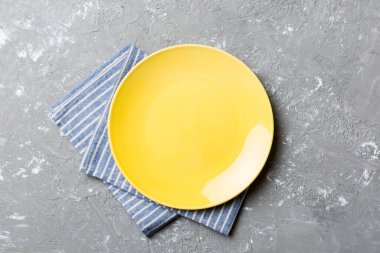 Renkli arka planda üst manzara. Yemek için masa örtüsü üzerinde boş yuvarlak sarı tabak. Tasarımınız için boşluk olan peçeteye boş tabak.