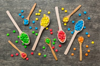 Renkli arka planda kaşık üzerinde renkli tatlı şekerler. Fotokopi alanı ile şekerleme dekoru üst görünümü.