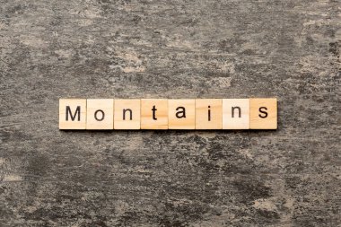 Ahşap bloğa yazılmış bir kelime. Dağlar çimento masa üzerinde metin desing, konsept için.